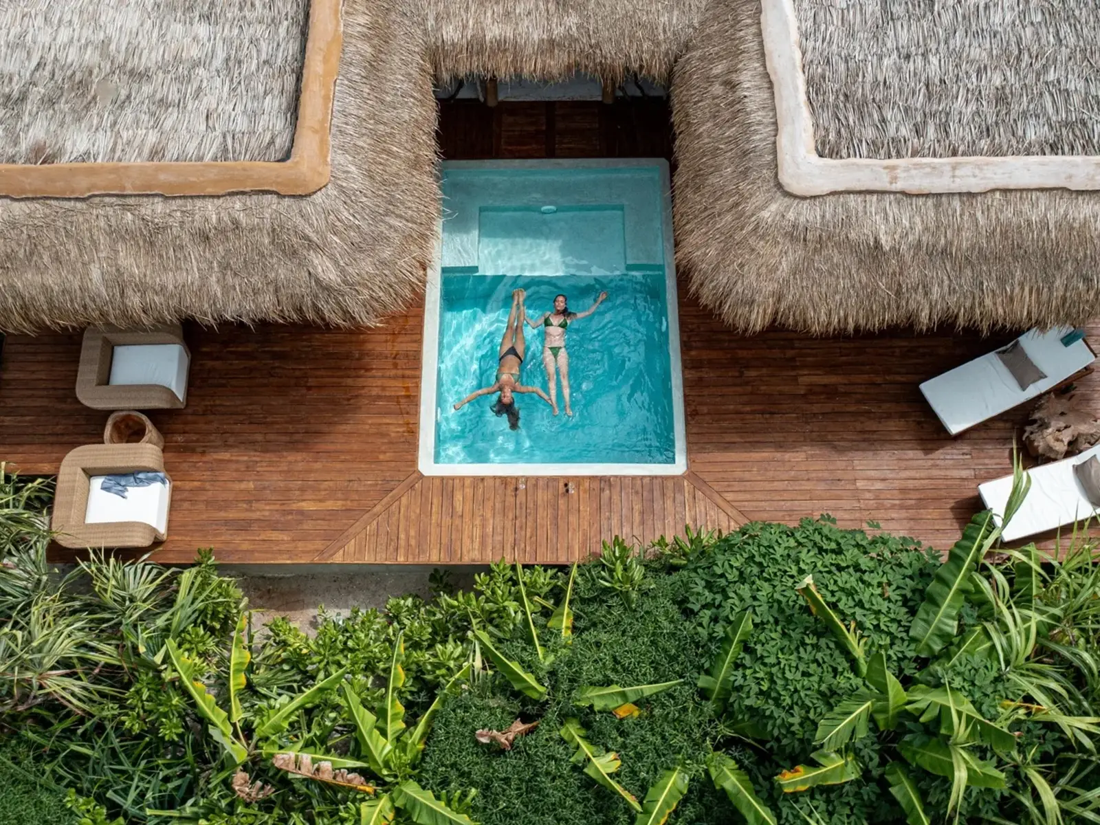 Two guests floating in the private plunge pool between two makuti-thatched villas at Sensations Eco-Chic Hotel, seen from above.