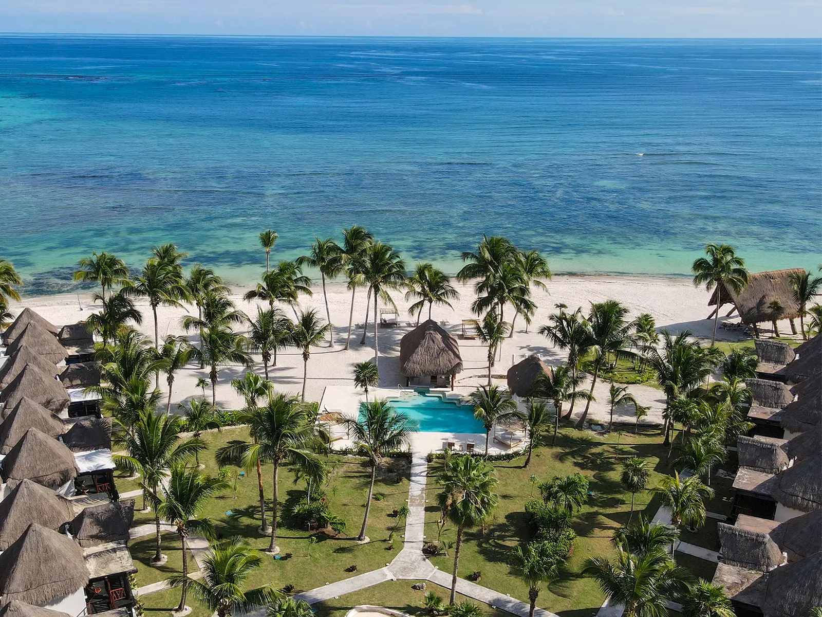 Aerial view of VR Club Tulum Riviera: palapa-roofed suites and a garden pool set behind a palm-lined white beach on the turquoise Caribbean.
