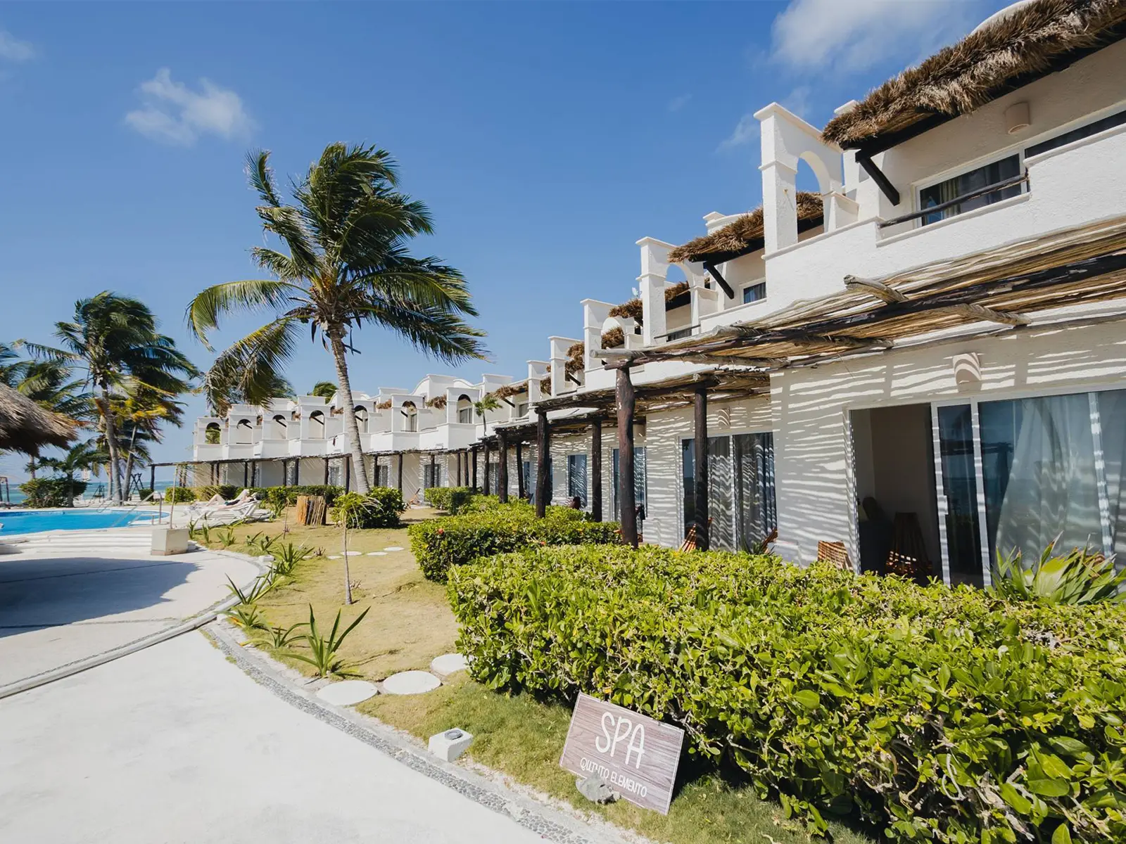 The seafront wing at VR Club Tulum Riviera: white suites under thatched pergolas, with the pool and gardens alongside.